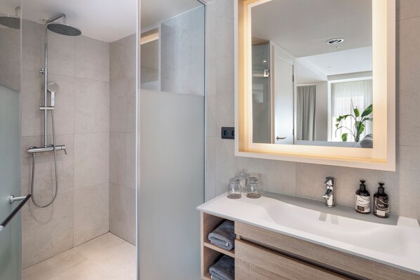 Un baño moderno con ducha envuelta en vidrio, un espejo grande y un lavabo con dos dispensadores de jabón.