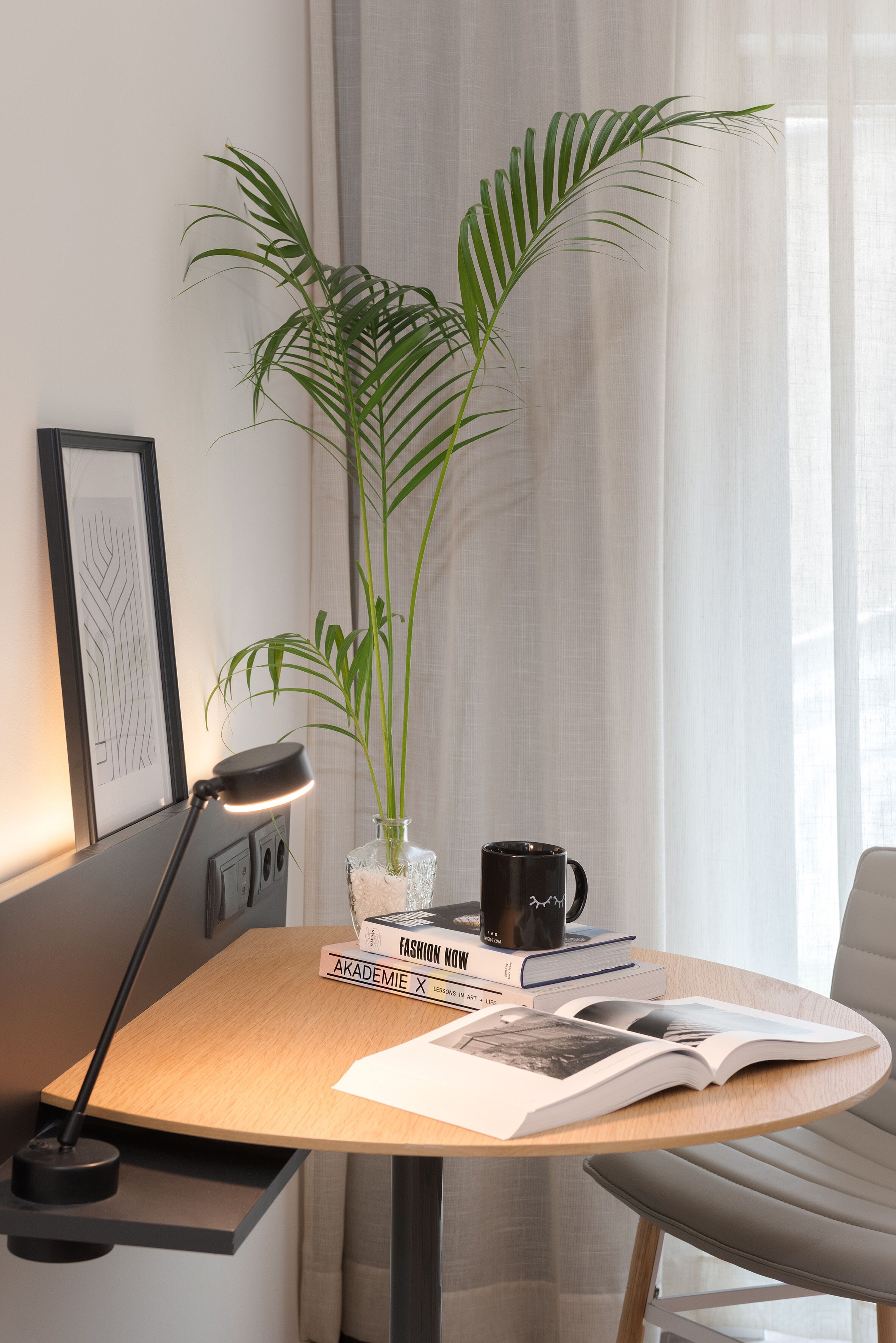 Un espacio de trabajo ordenado con escritorio, lámpara, planta en maceta, taza y libros.