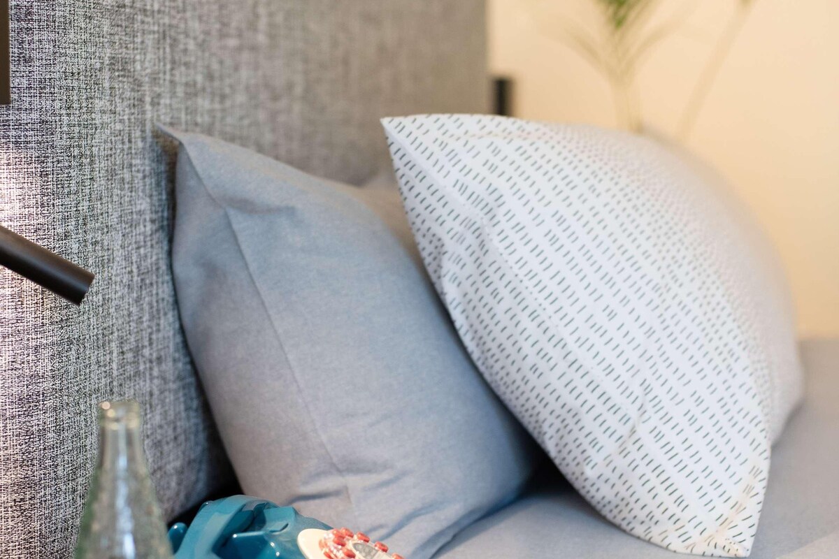 Ein modernes Wohnzimmer mit einem grauen Sofa, einem runden Holztisch, einem blauen dekorativen Element und einem Glas Wasser.