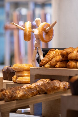 Une exposition de divers produits de boulangerie, notamment des beignets, des croissants, et une figurine en bois tenant en équilibre un beignet.