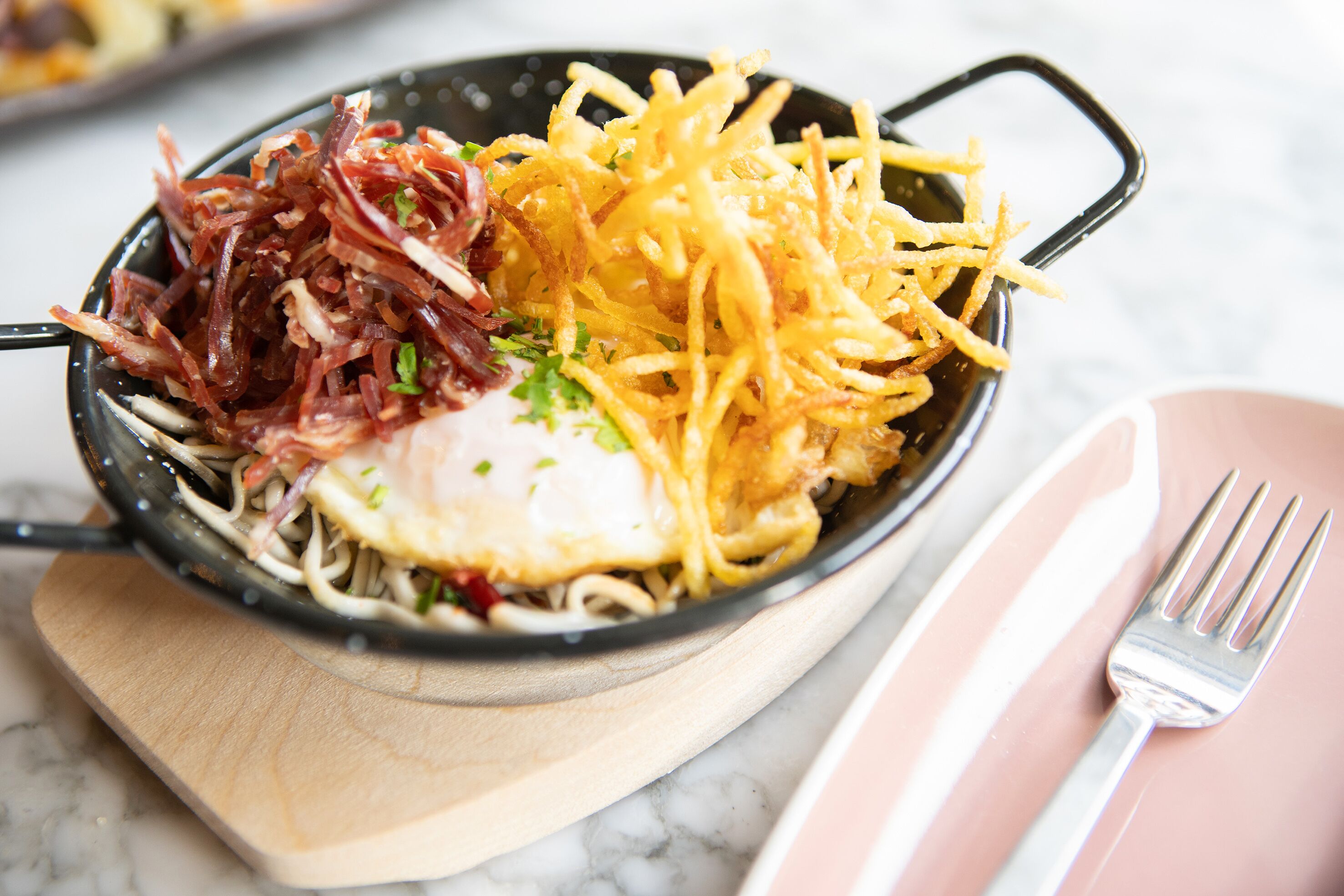 Una ciotola di cibo con noodles, carne sfilacciata e formaggio su un tagliere di legno.