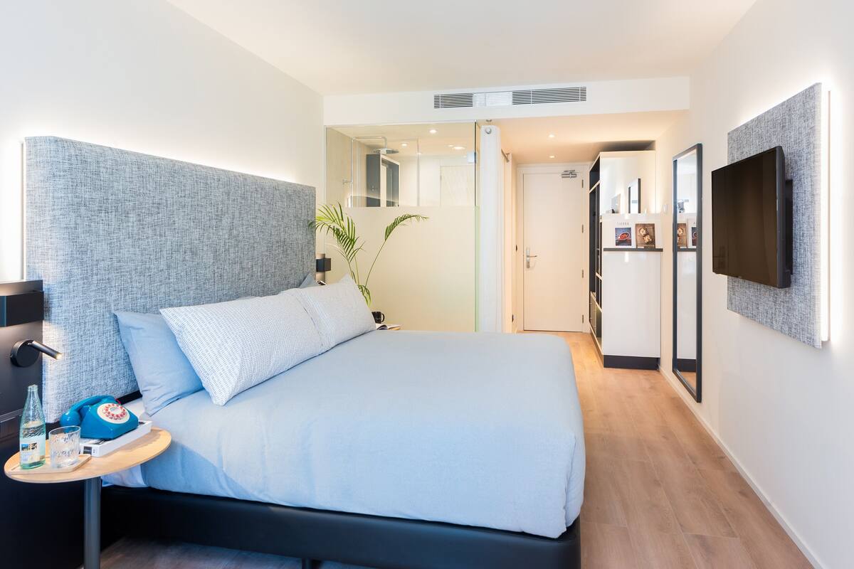 Una habitación de hotel moderna con una cama grande, mesita de noche y televisor de pantalla plana montado en la pared.