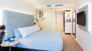 Una habitación de hotel moderna con una cama grande, mesita de noche y televisor de pantalla plana montado en la pared.