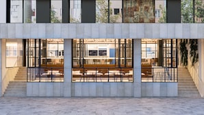 Un edificio moderno con amplios ventanales, una escalera y un área de descanso con mesas y sillas.