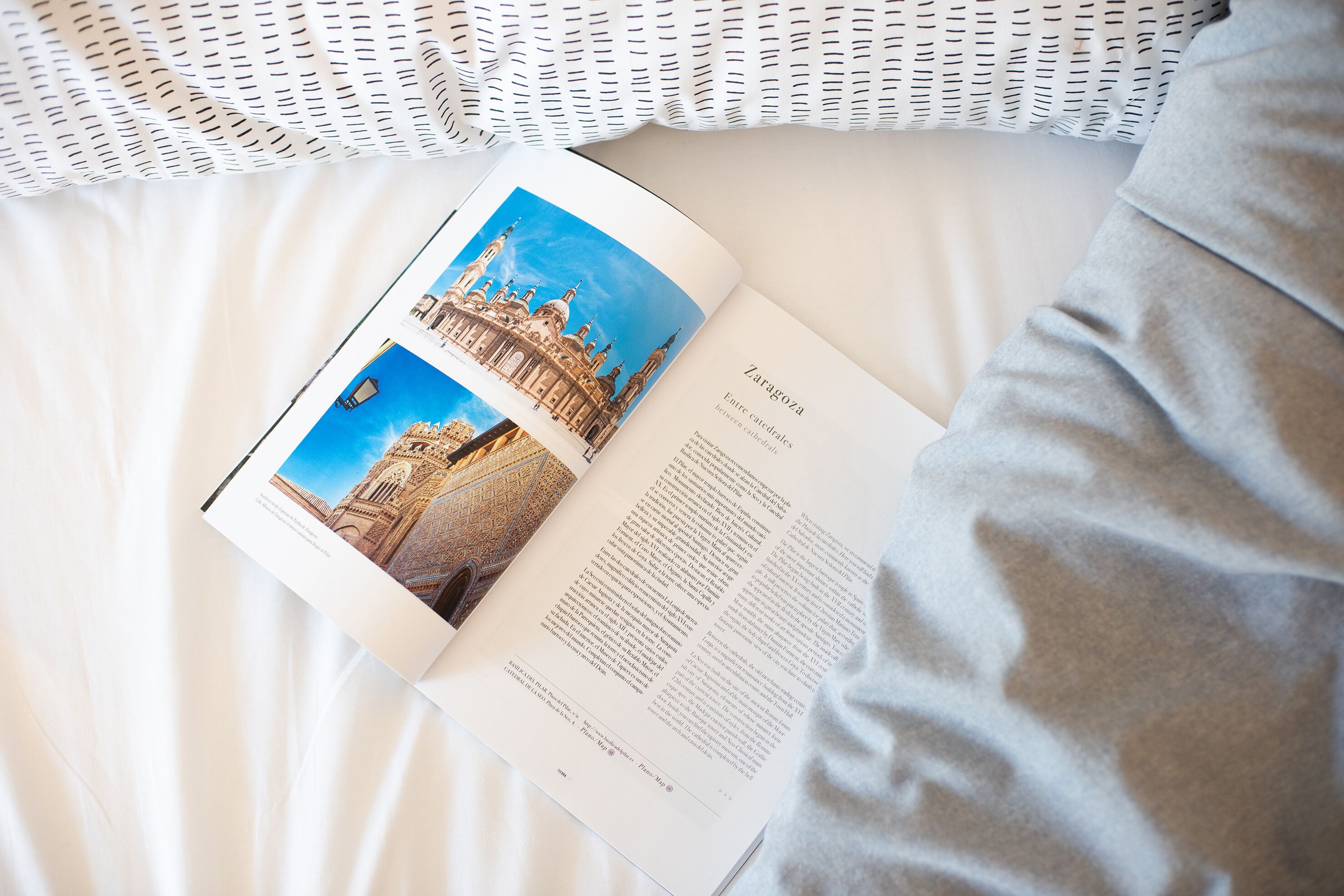 A book open on a bed with a page featuring a building and text about Zaragoza.