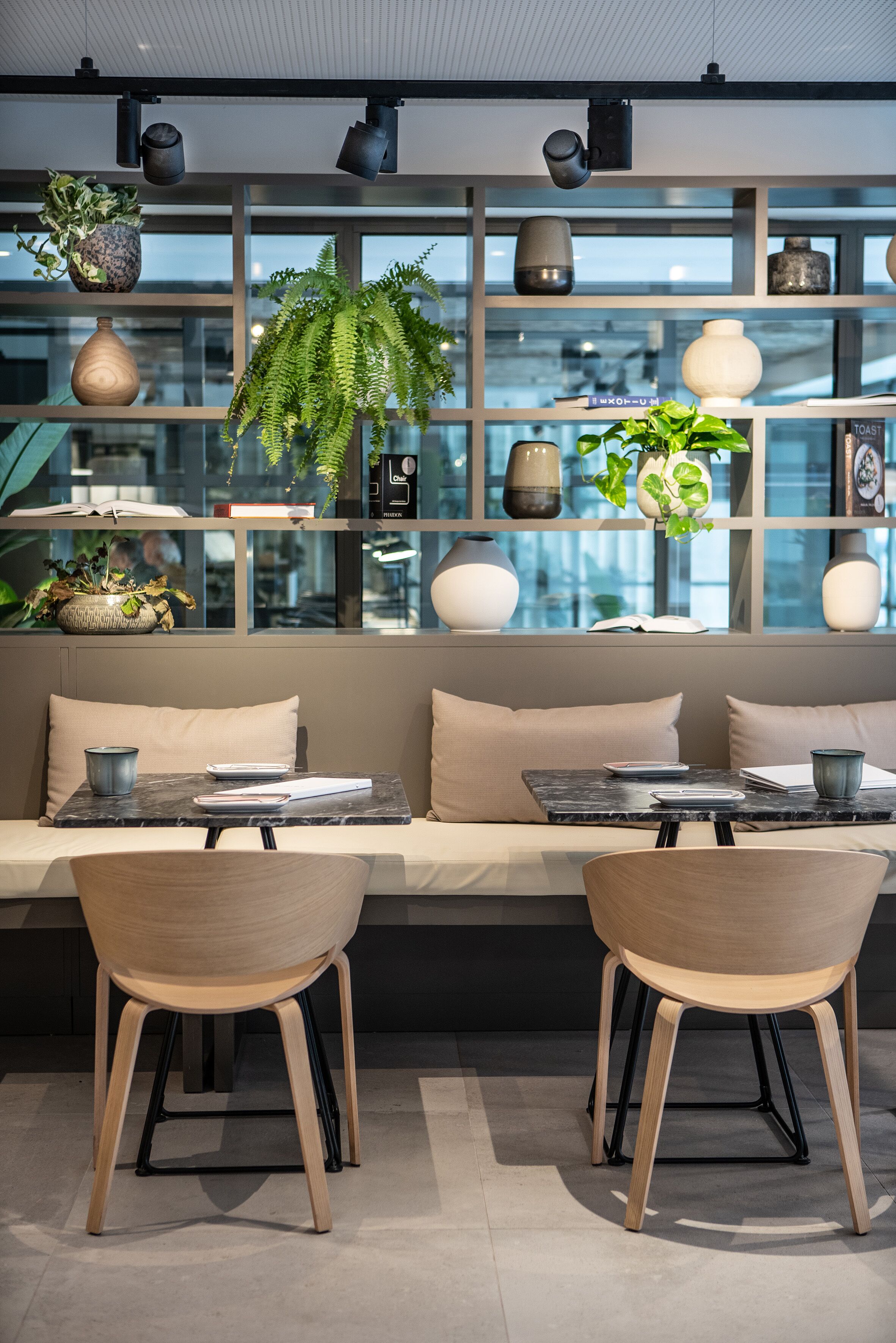 Un interior moderno con una zona de estar que incluye un sofá y dos sillones, una mesa con cubierta de mármol y un aparador con objetos decorativos y plantas.