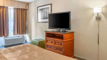 A hotel room with a bed, a wooden dresser, a television, a framed picture on the wall, and a window with curtains.