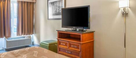 Une chambre d’hôtel avec un lit, une commode en bois, un téléviseur, un tableau encadré au mur et une fenêtre avec des rideaux.