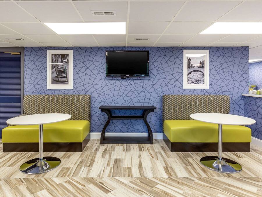 A reception area with a blue patterned wall, a flat-screen TV mounted above a black console table, and two yellow cushioned seating areas with round tables.