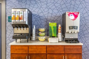 Un área de bebidas con varios dispensadores, incluyendo una máquina de Nescafé y un dispensador de jugo fresco.