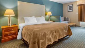 A hotel room with a large bed, two bedside tables with lamps, a small bench, and a framed picture on the wall.