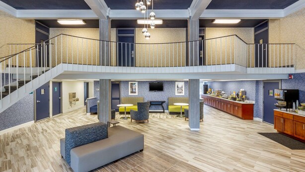 A spacious lobby with a high ceiling, a staircase leading to an upper level, seating areas, and a reception desk.