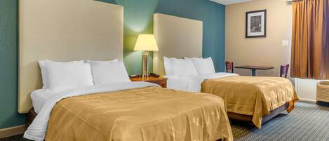 A hotel room with two beds, a small table, a lamp, and a framed picture on the wall.