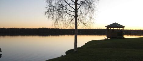 A gazebo by a calm lake at sunset.