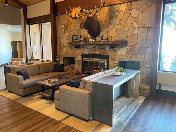 A cozy living room with a stone fireplace, a mounted moose head, and a modern sofa set. - Best Western Lake Lucille Inn (Wasilla)