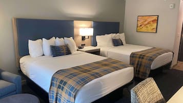 A hotel room with two beds, a desk, a chair, and a lamp.