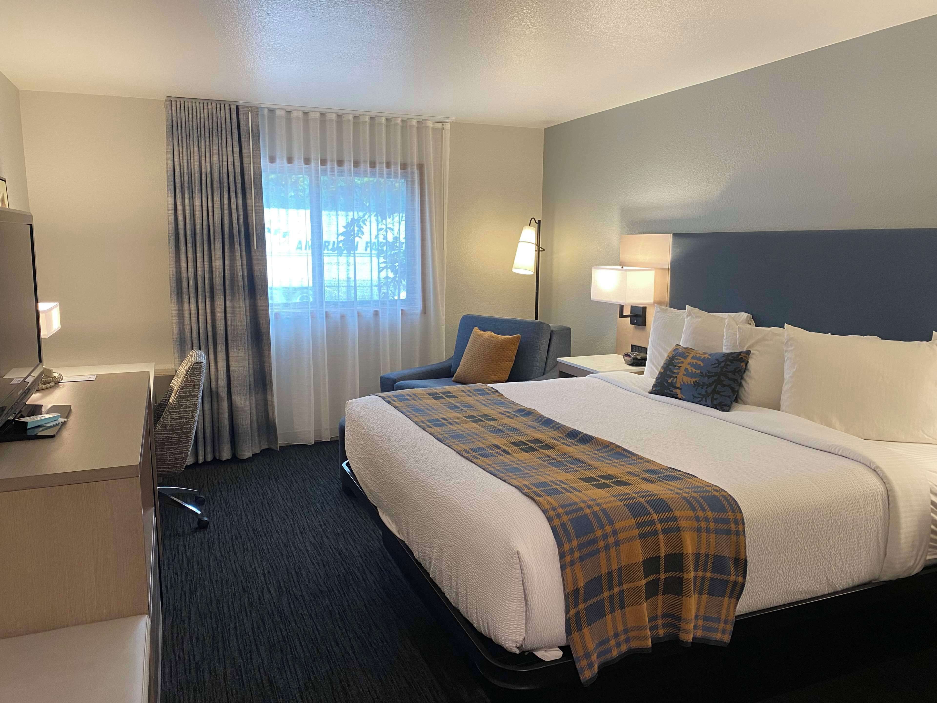 A hotel room with a large bed, a desk, a chair, and a window with curtains.
