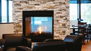 A stone fireplace with a fire, surrounded by leather chairs in a dining area. - Best Western Lake Lucille Inn (Wasilla)