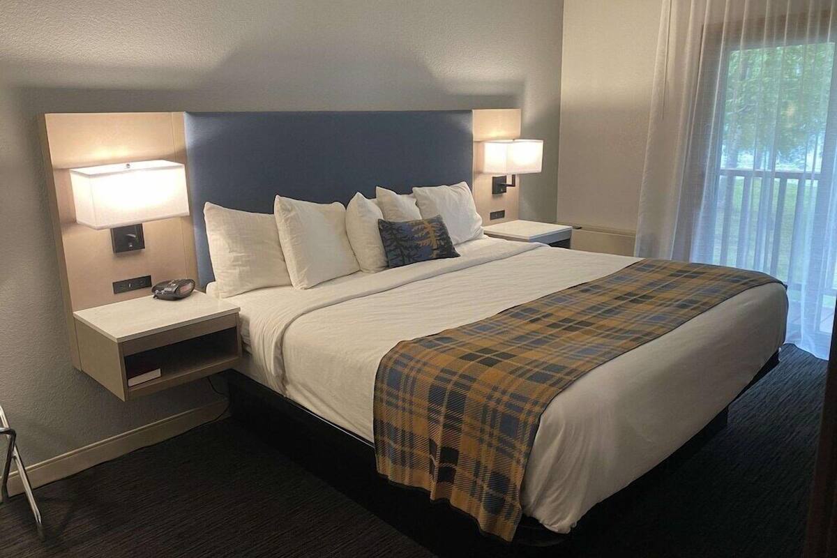 A hotel room with a large bed, two bedside tables with lamps, a headboard, and a window with curtains.
