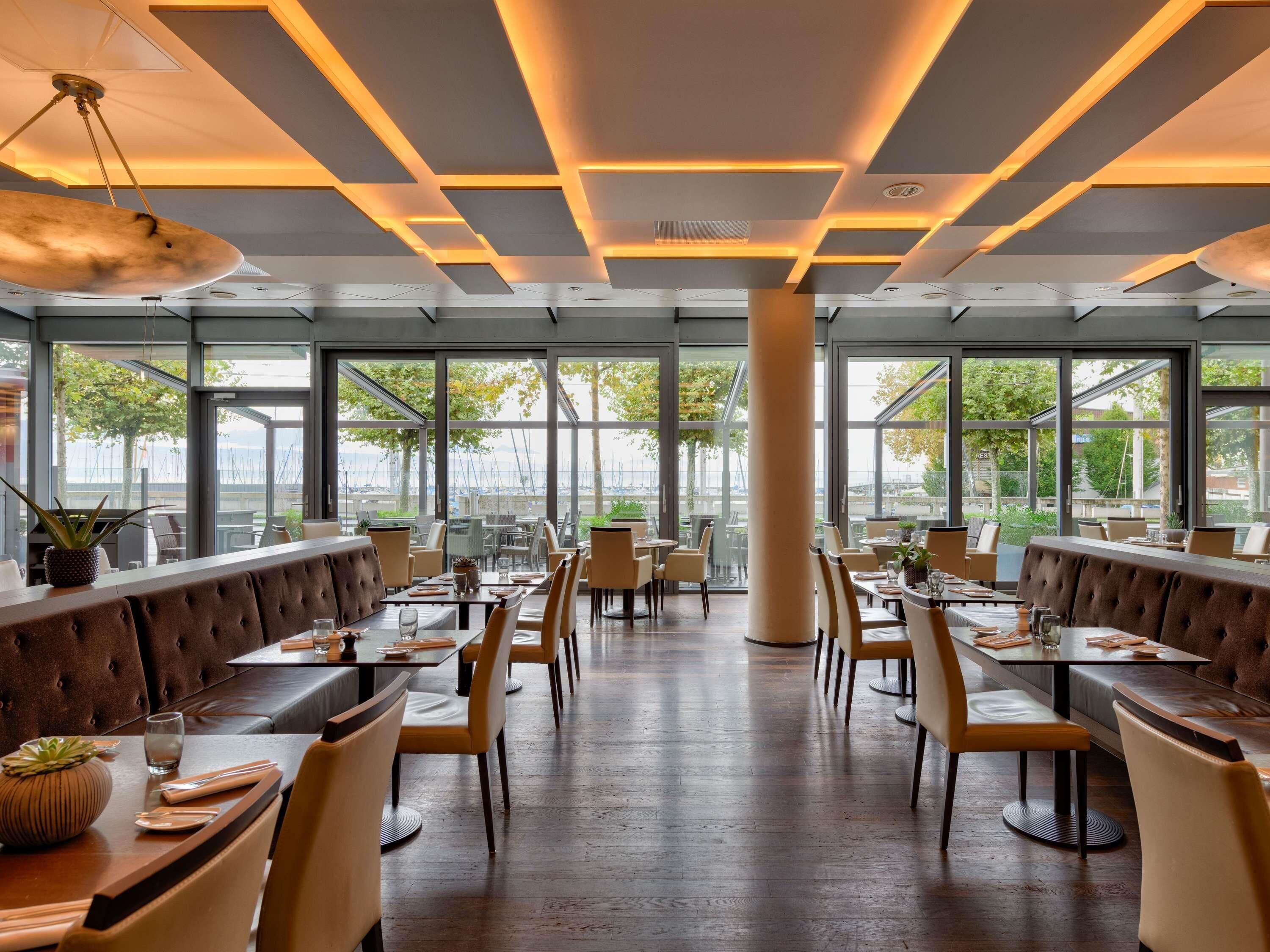 A modern restaurant with high ceilings, large windows, and a central column.