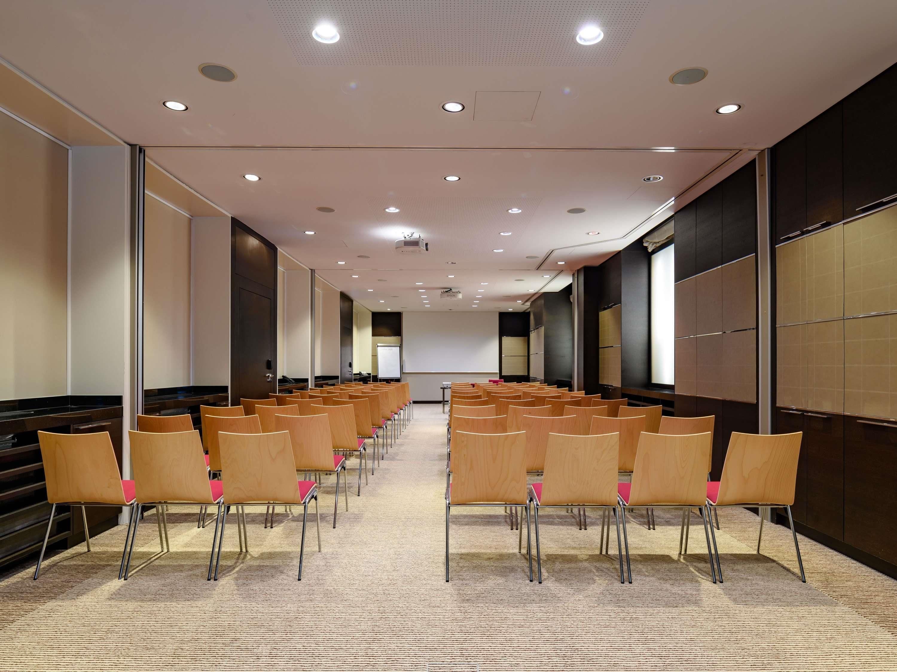 A conference room with rows of chairs, a projector screen, and a carpeted floor.