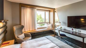 A hotel room with a bed, a desk, a chair, a TV, and a window with curtains.