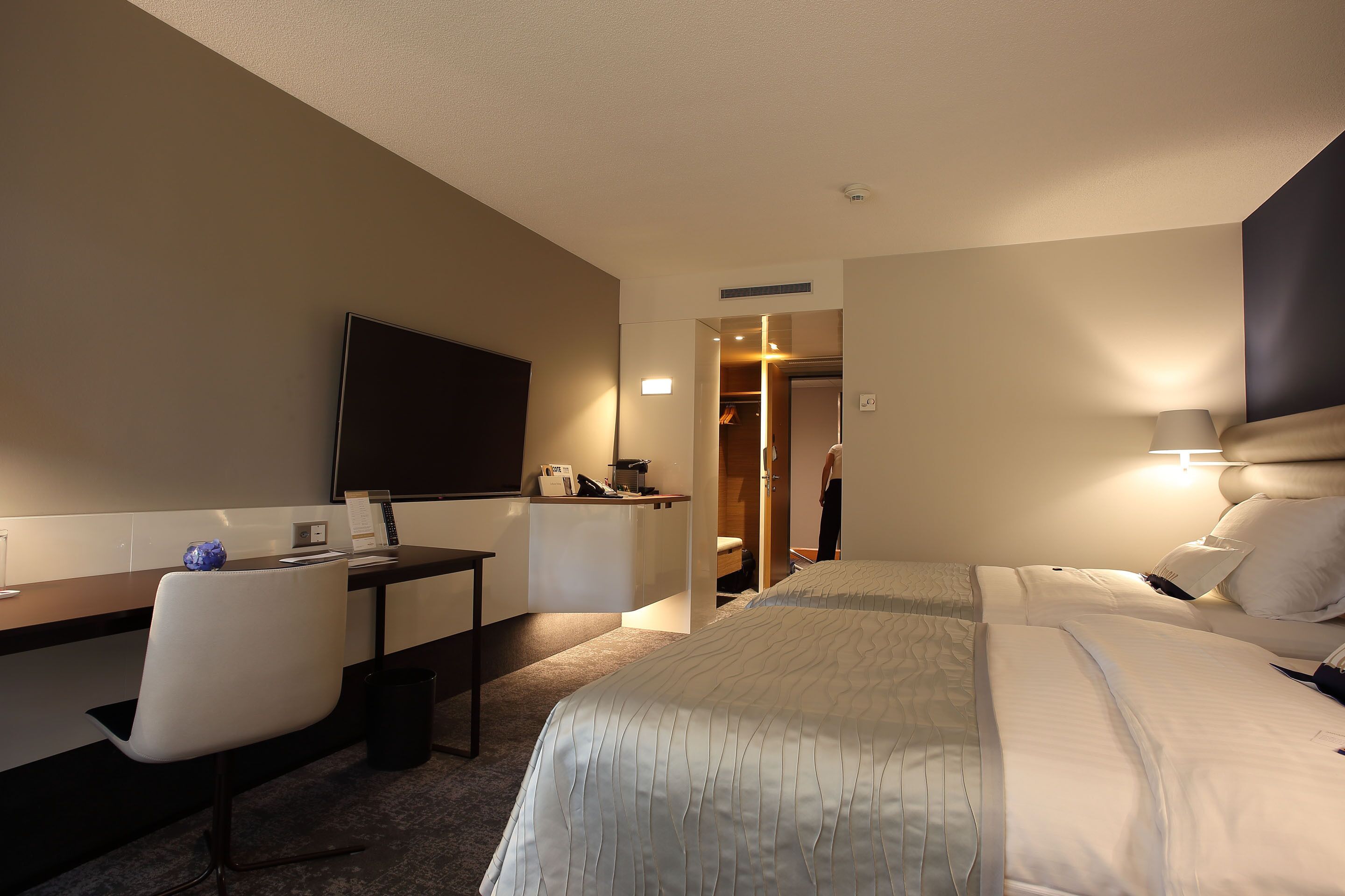 Habitación de hotel con cama, escritorio con silla, televisor y baño visible a través de una puerta abierta.