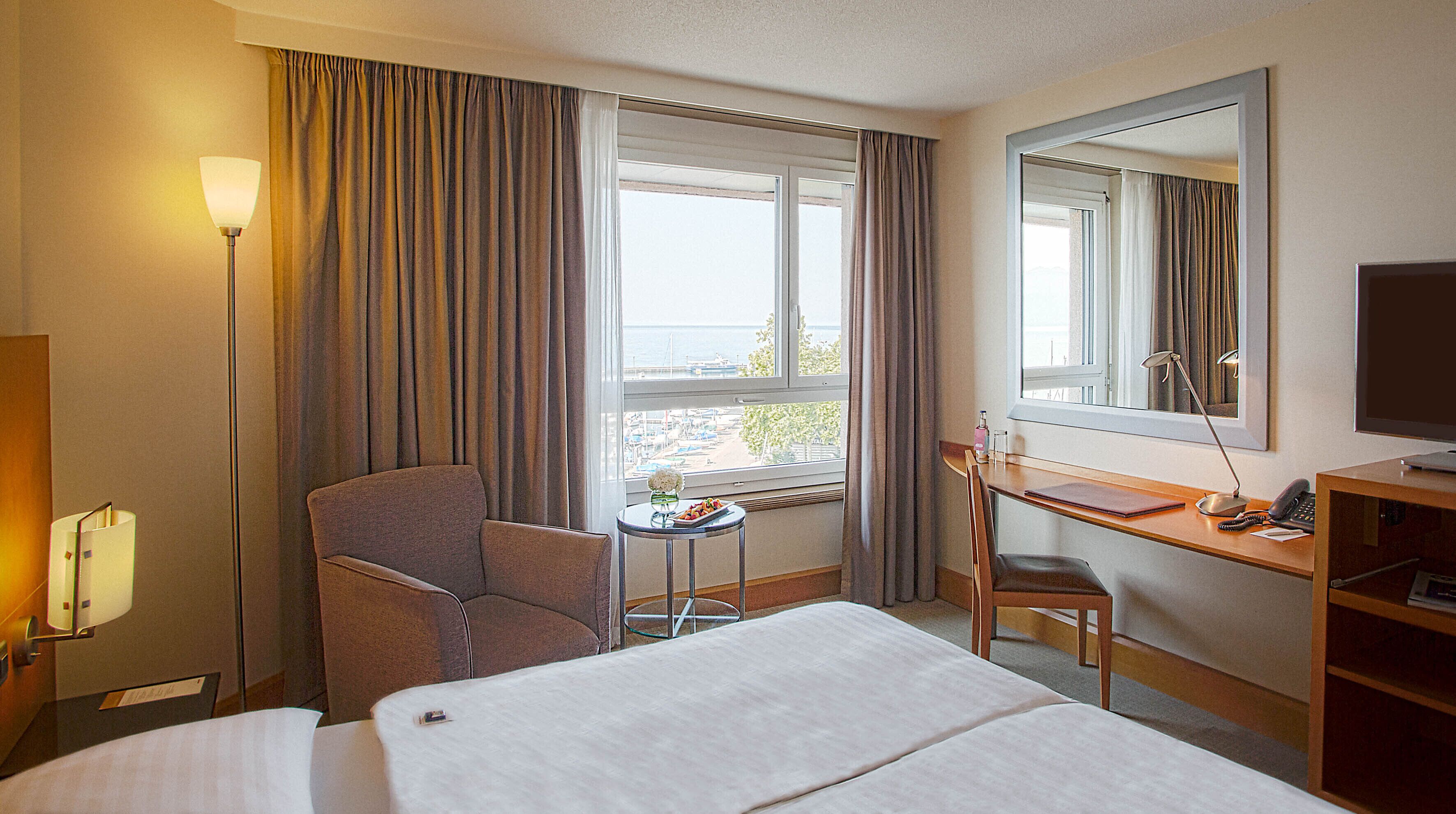 Une chambre d’hôtel avec un lit, un bureau, une chaise et une grande fenêtre avec des rideaux.