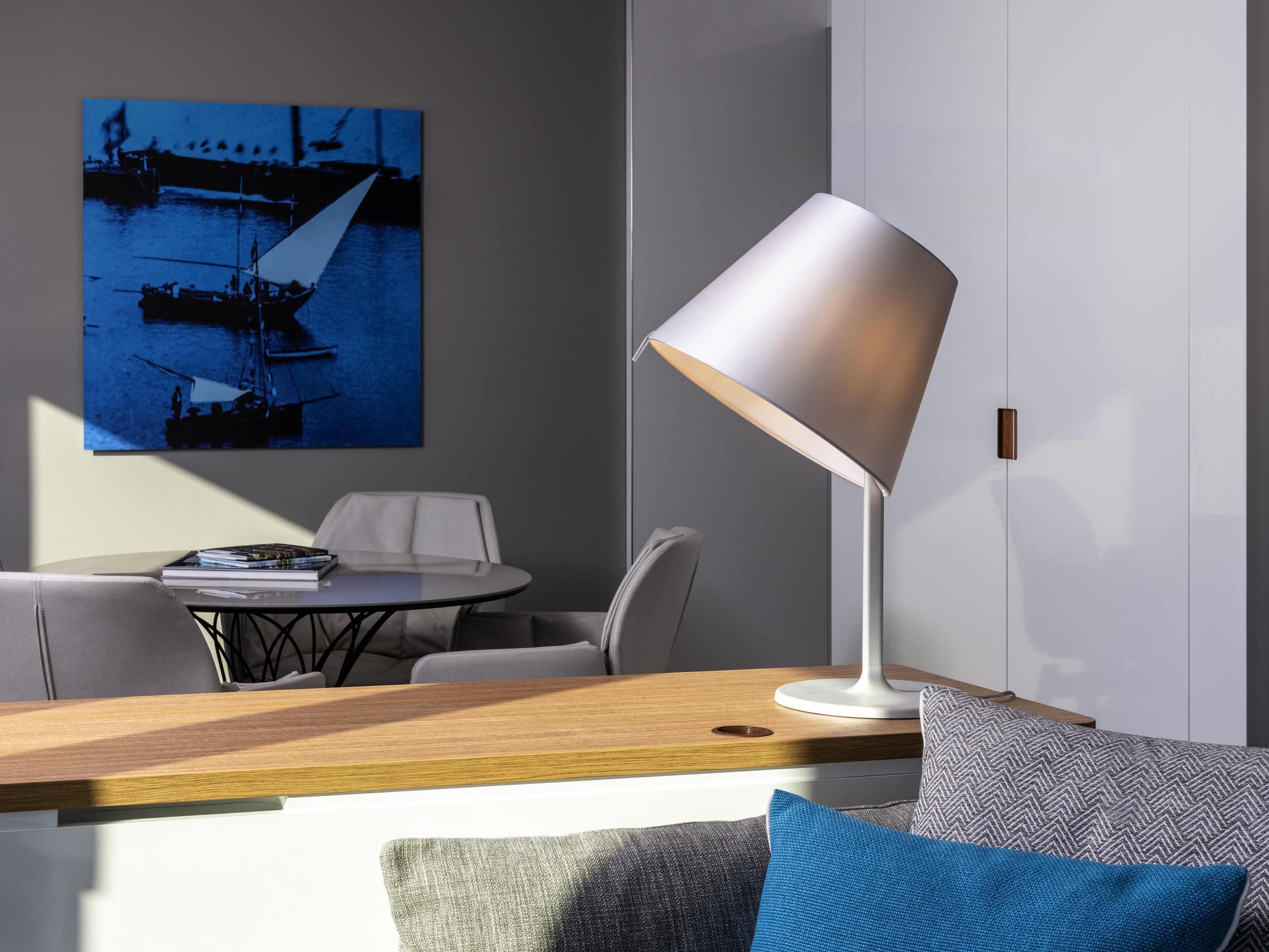 A modern room with a desk, a chair, a table, a lamp, and a painting on the wall.
