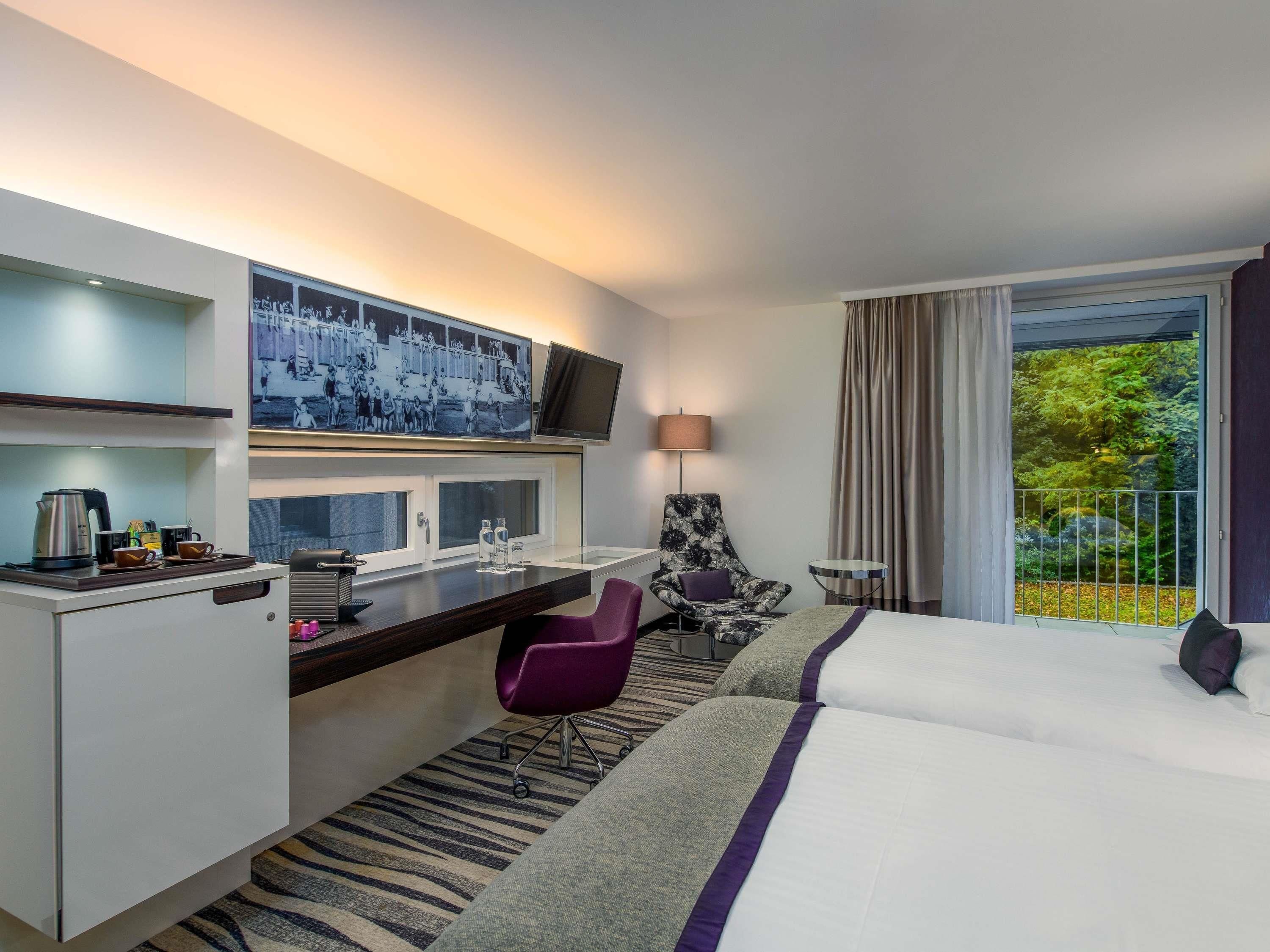 Een hotelkamer met een bed, een bureau met stoel, een televisie en een raam met gordijnen.