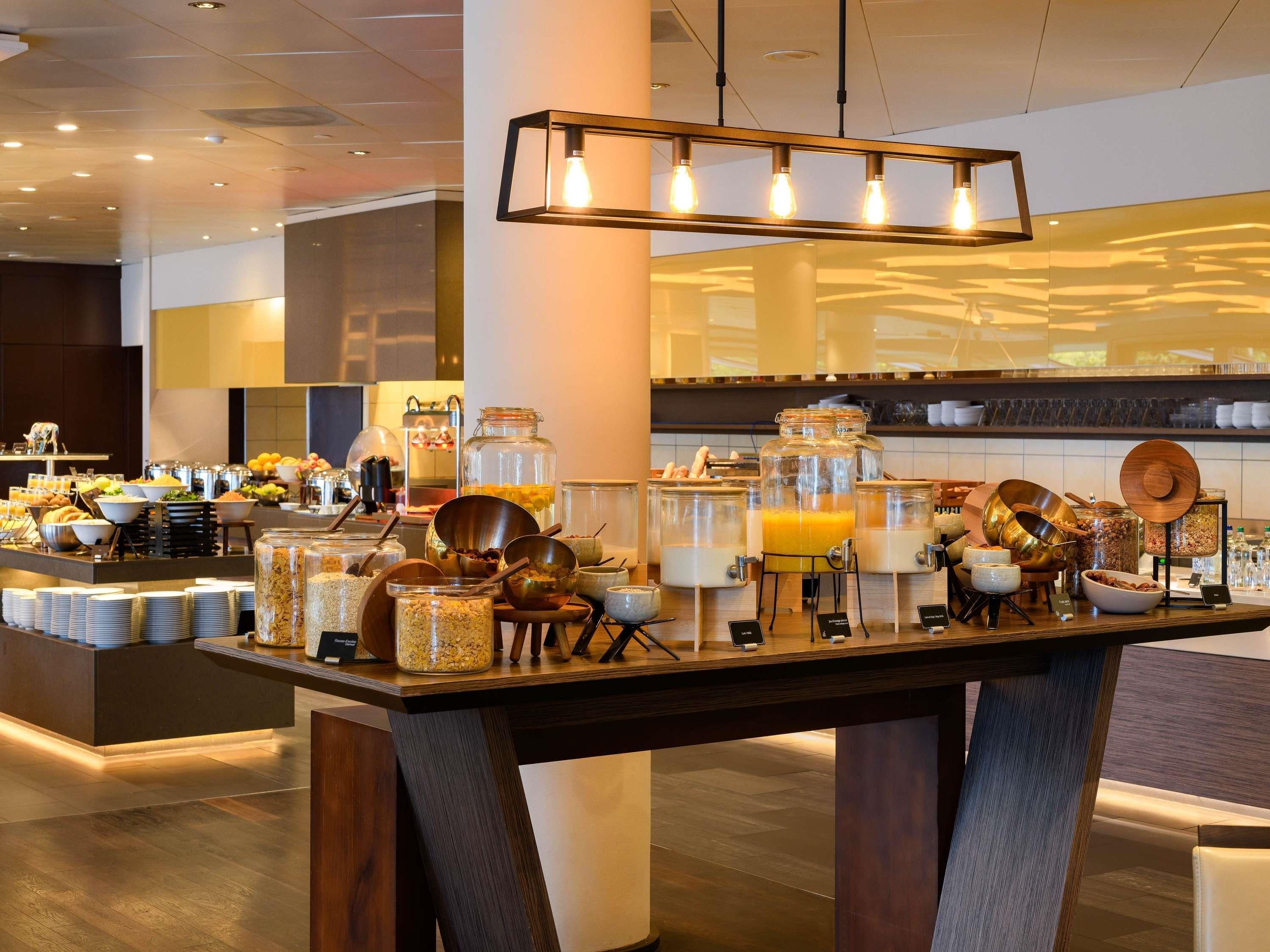 Un buffet de petit-déjeuner proposant une variété d’aliments et de boissons, notamment des fruits, des céréales et des jus, le tout présenté dans un cadre moderne d’hôtel.