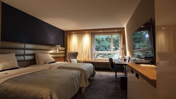 Quarto de hotel com duas camas, uma escrivaninha, uma cadeira, uma televisão e uma janela com cortinas.