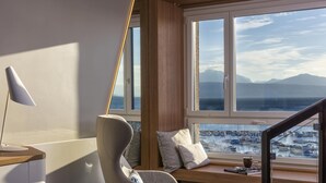 Habitación moderna con vista al mar, un sillón cómodo, un escritorio con lámpara y una escalera.