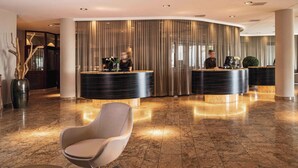 Een moderne lobby met een receptiebalie, een gebogen muur en een zithoek met een stoel en een ronde tafel.