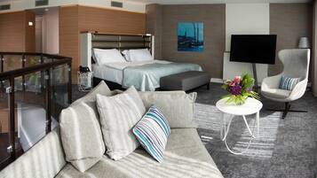 Habitación de hotel moderna con cama, sofá, televisor y barandilla de vidrio.