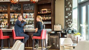 A bar area with a bartender, a woman seated, and a man seated at a bar counter. There are multiple bottles and glasses on shelves, and a laptop on a counter.