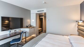 Ein Hotelzimmer mit Bett, Schreibtisch, Stuhl, Fernseher, Dusche und Toilette.