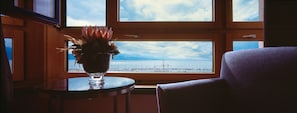 Une pièce dotée d’une grande fenêtre donnant sur un port de plaisance, avec une plante en pot sur une table et une chaise placée face à la fenêtre.