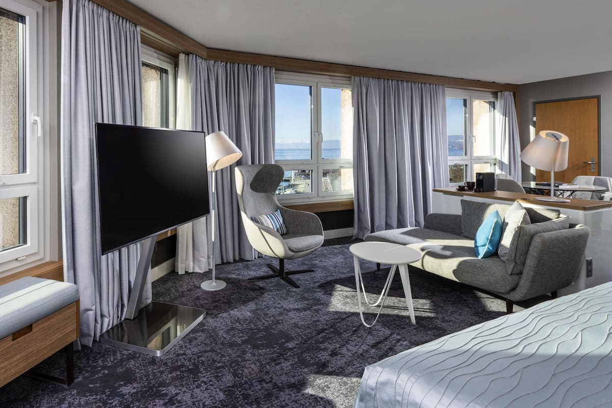 Een hotelkamer met een grote televisie, een bank, een stoel, een klein tafeltje en een bed.