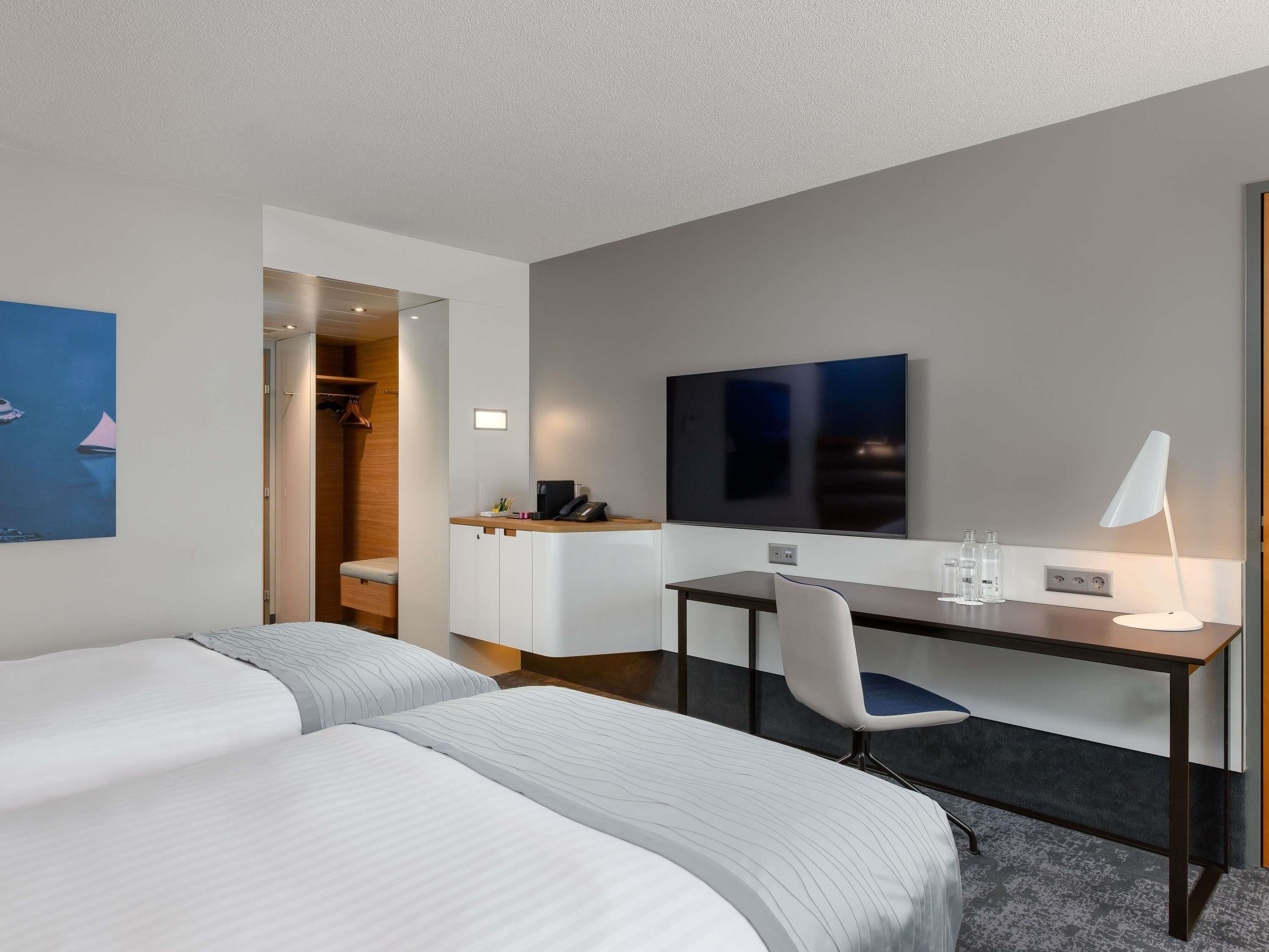 Habitación de hotel con dos camas, un escritorio, una silla, un televisor y zona de ducha.