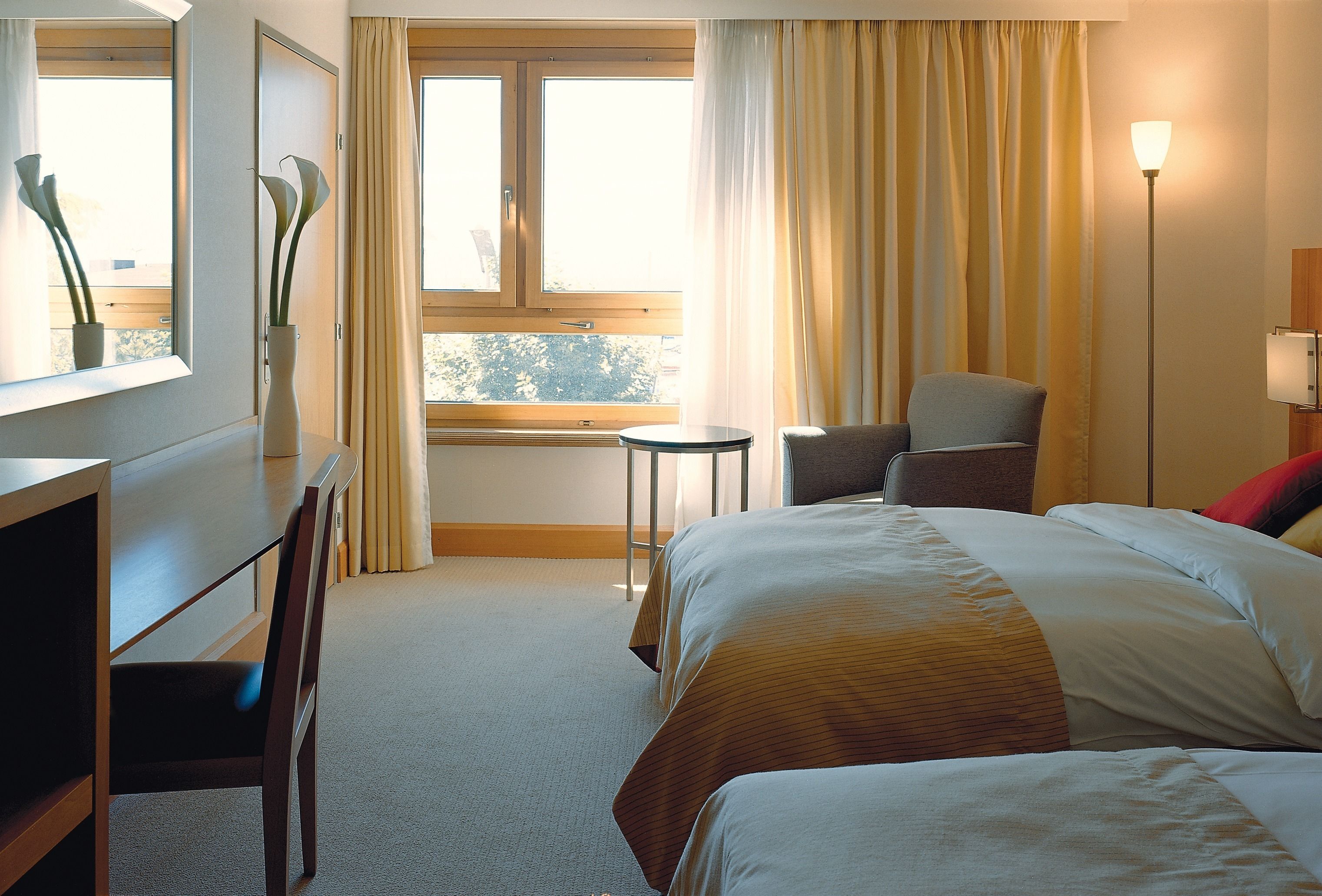 Una habitación de hotel con una cama, un escritorio, una silla, una mesita y una lámpara.