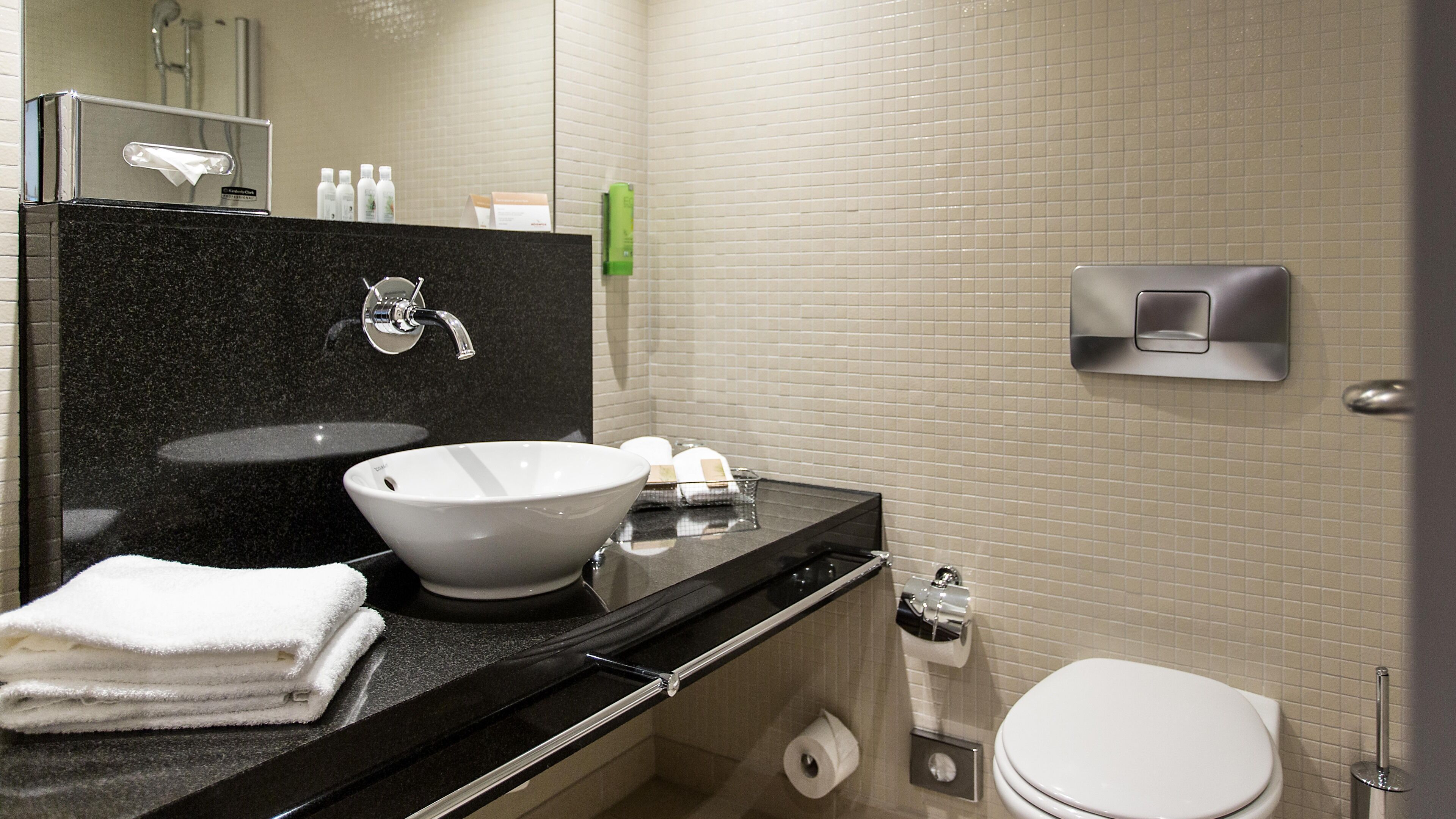 A modern bathroom with a black countertop, a white sink, a mirror, a toilet, and a hand dryer.