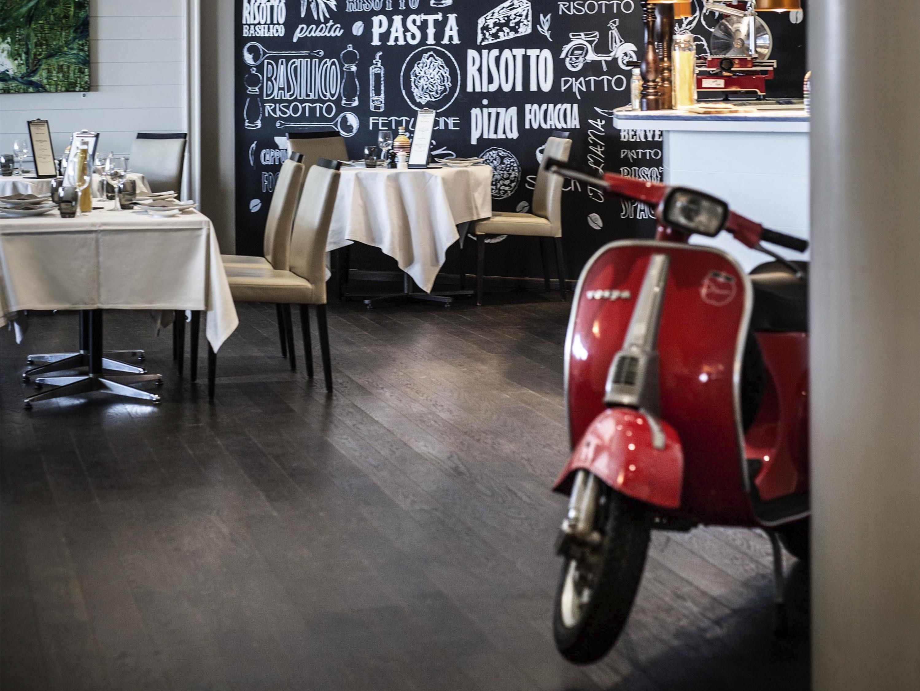 Un interior de restaurante con mesas, sillas, una scooter roja y una pared con palabras relacionadas con la comida.