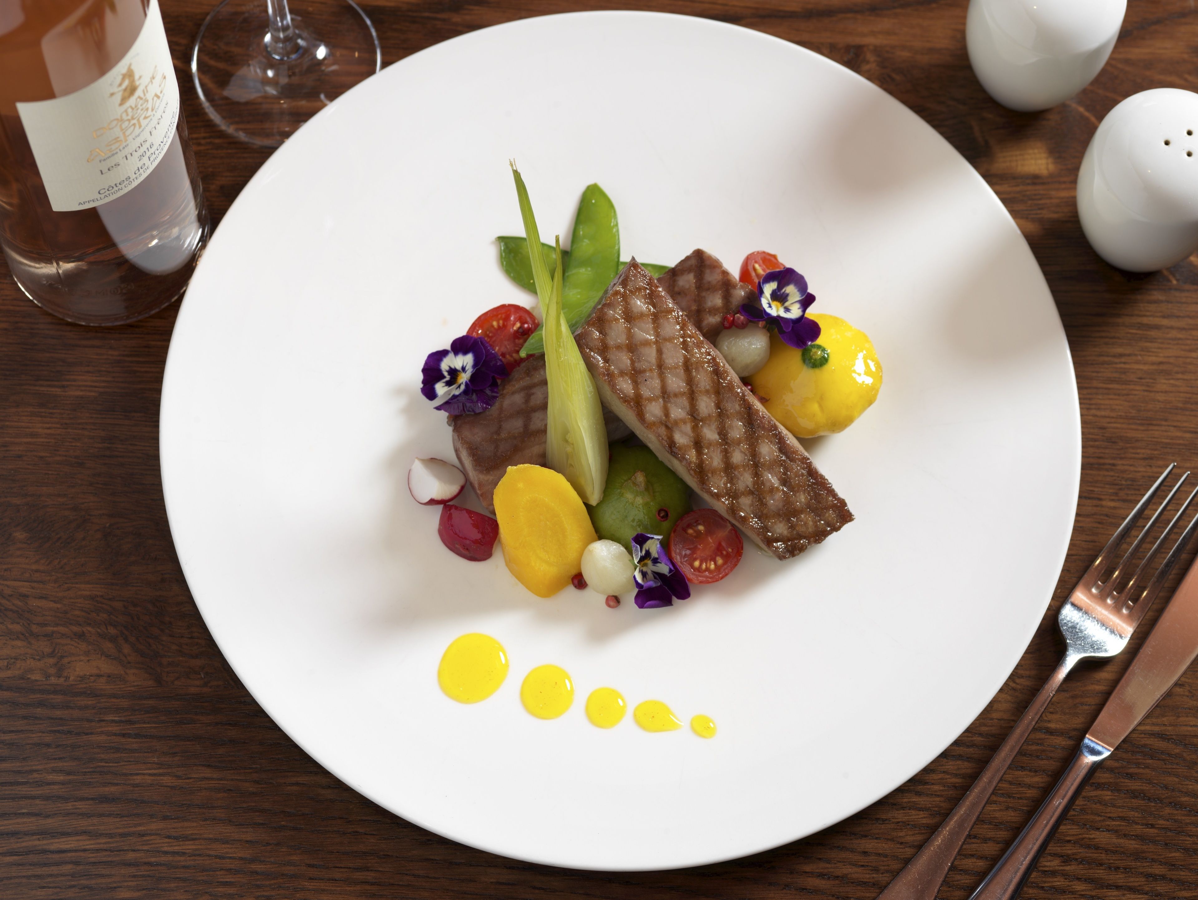 A white plate with a piece of grilled meat, vegetables, and a decorative sauce.