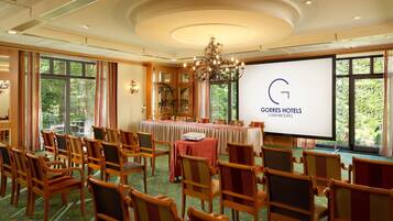 A conference room at Goeffes Hotels in Luxembourg with wooden chairs, a large screen, and a chandelier.