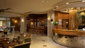 Rebuda d'hotel amb taulell de recepció, zona de bar i seients decorats amb arranjaments florals.