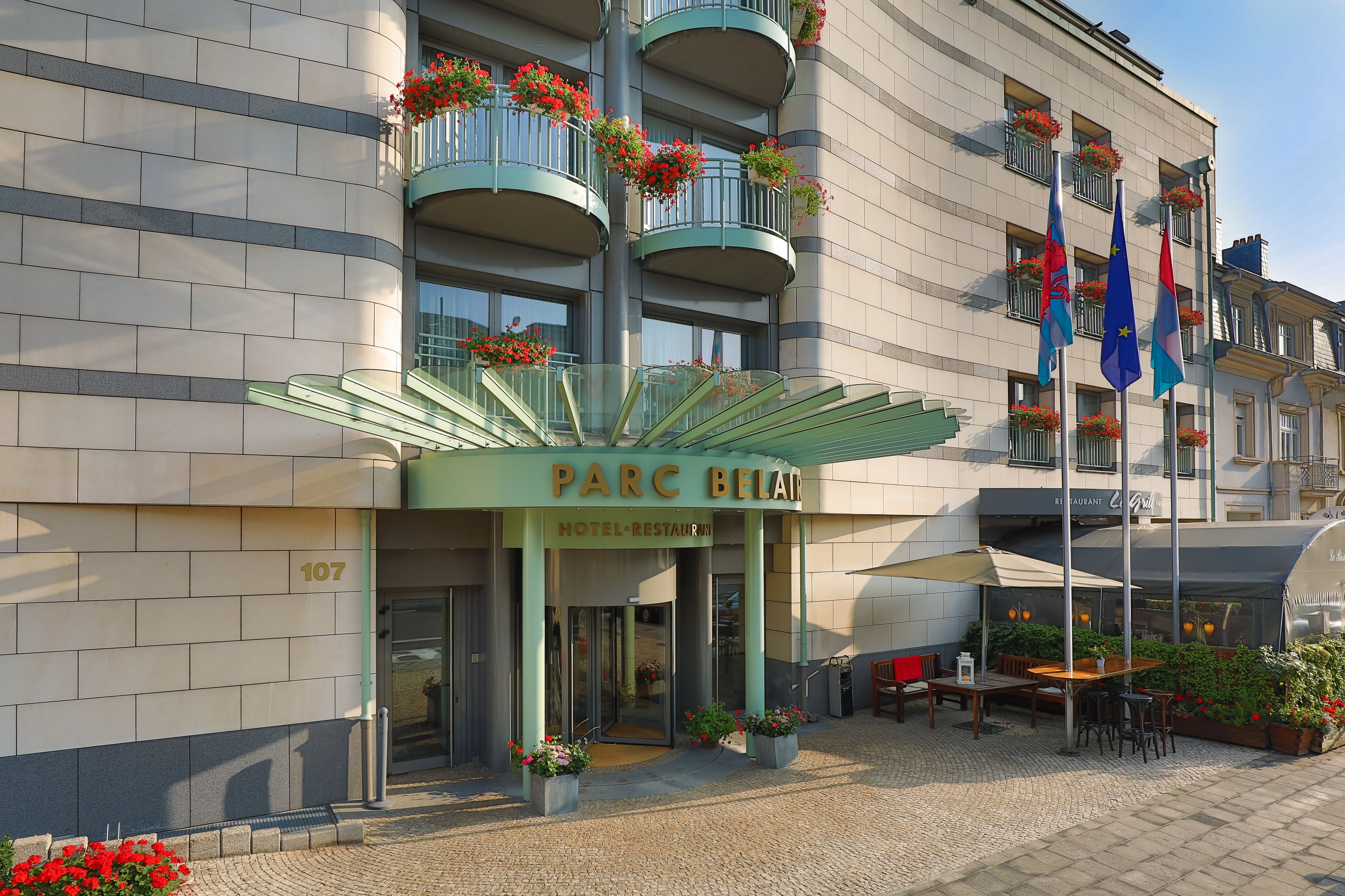 Een hotelentree met een groen luifel, terrasstoelen en vlaggen.