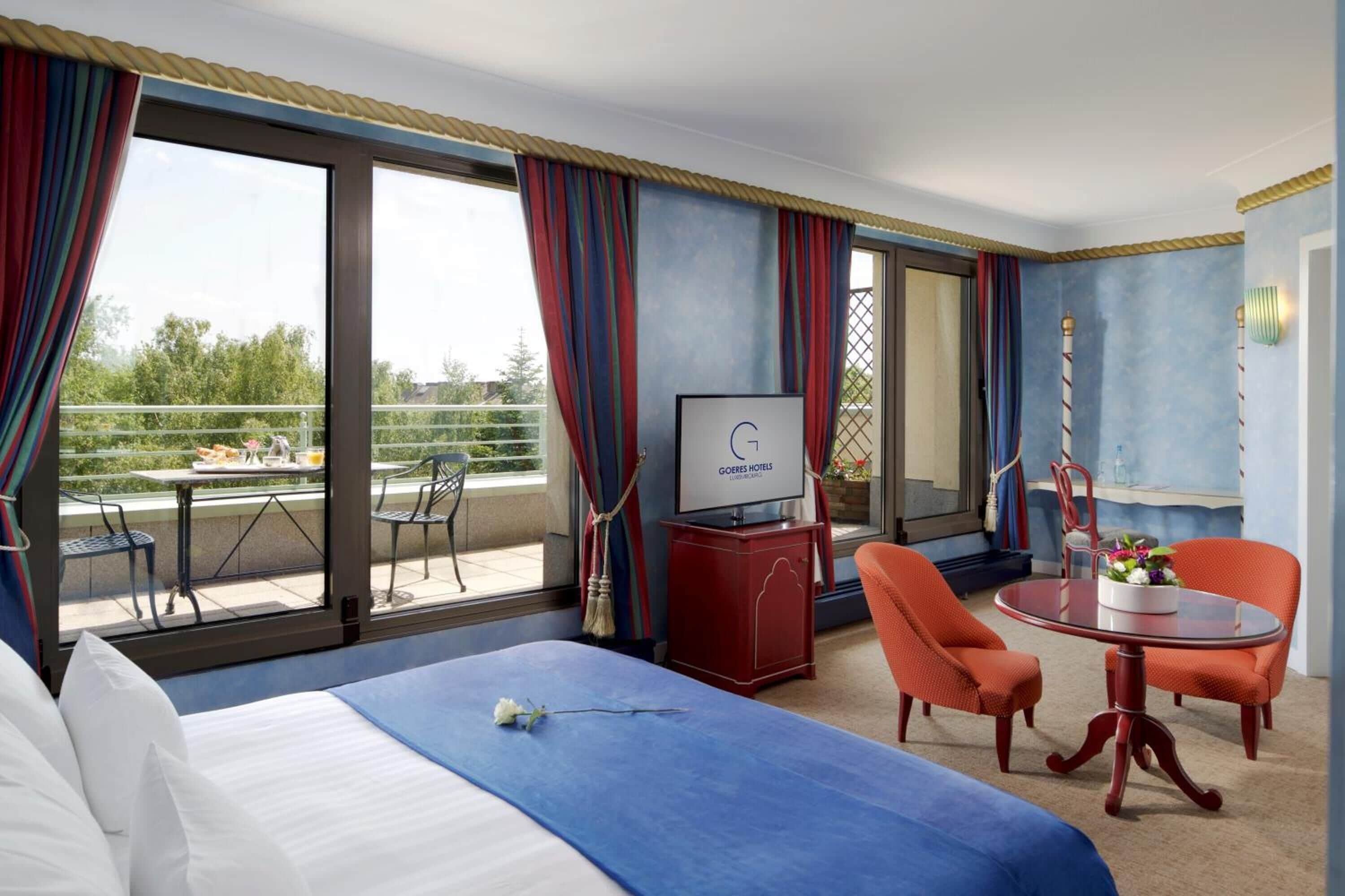 A hotel room with a bed, a desk, a chair, a table, and a view of the outdoors.
