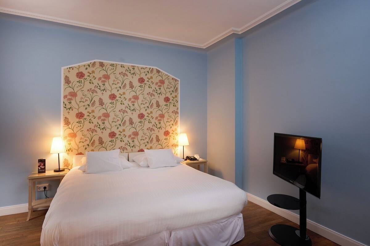 Een hotelkamer met een groot bed, twee bedlampen, een flatscreen televisie en bloemenbehang.
