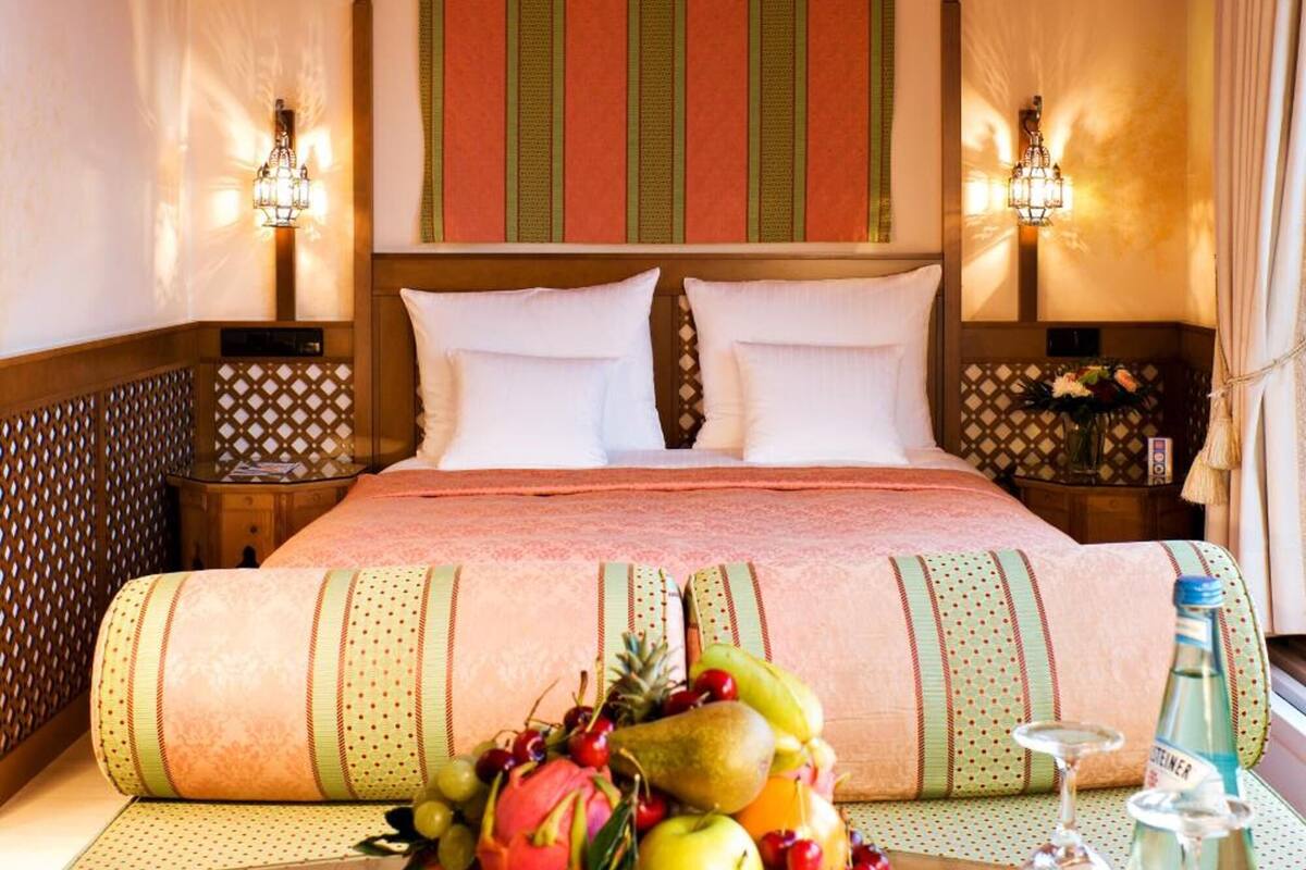Een hotelkamer met een groot bed, een houten nachtkastje, een tafel met fruit en glazen, en een decoratief baldakijn.